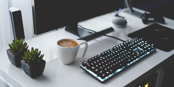 a clean white desk with monitor, keyboard, cup of coffee and two small plants